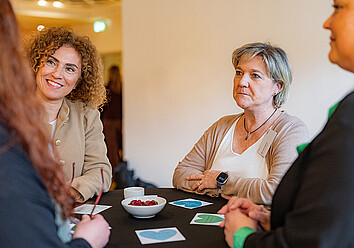 Mehrere Personen stehen um einen Bistrotisch und unterhalten sich Mehrere Personen stehen um einen Bistrotisch und unterhalten sich