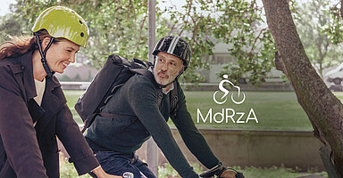 Mit dem Rad zur Arbeit: Eine junge Frau und ein älterer Mann radeln durch einen Park Mit dem Rad zur Arbeit: Eine junge Frau und ein älterer Mann radeln durch einen Park