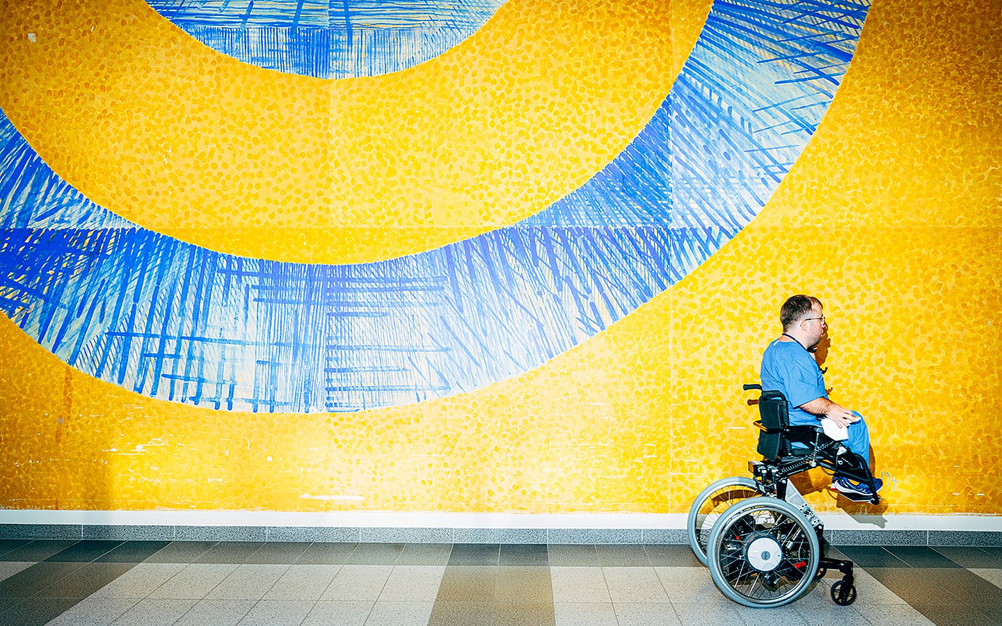 Foto von Charité-Arzt Dr. Leopold Rupp, wie er mit seinem Rollstuhl an einer blau-gelben Wand vorbeifährt