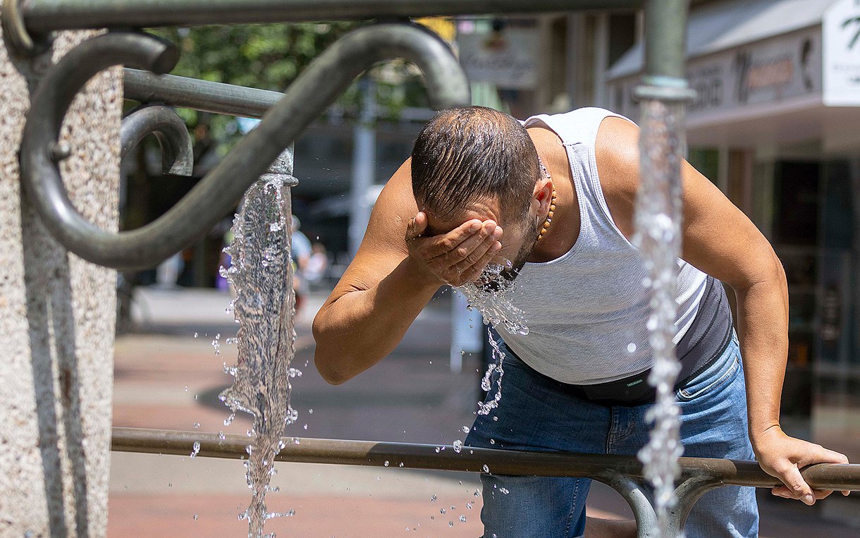 Foto eines Mannes, der sich bei Hitze Wasser ins Gesicht spritzt.