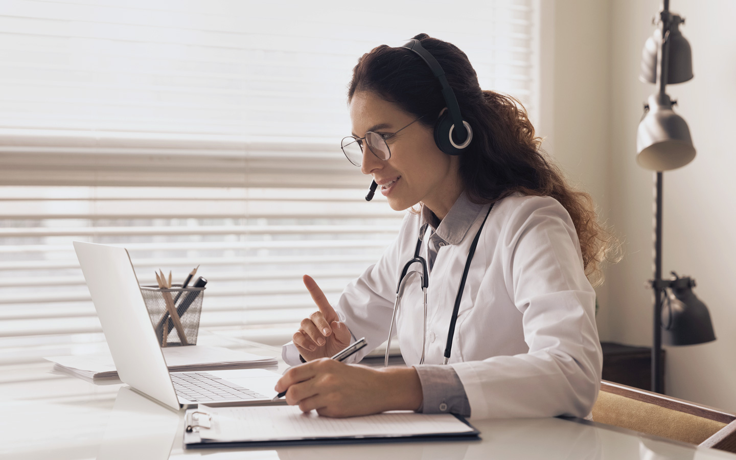 Foto: Ärztin sitzt vor einem Laptop und trägt ein Headset.