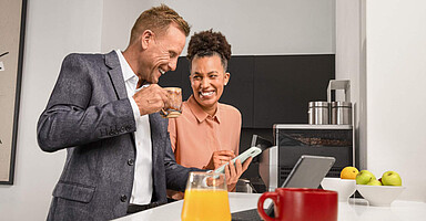 AOK atWork: Zwei Menschen schauen in einer Büroküche gemeinsam auf ein Smartphone, umgeben von gesunden Lebensmitteln AOK atWork: Zwei Menschen schauen in einer Büroküche gemeinsam auf ein Smartphone, umgeben von gesunden Lebensmitteln
