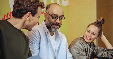 Diversität im Unternehmen: Drei Teammitglieder im freundlichen Austausch Diversität im Unternehmen: Drei Teammitglieder im freundlichen Austausch