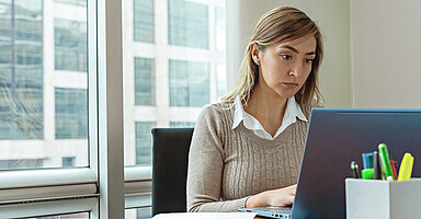 Betriebsprüfung: Junge Frau sitzt im Büro und blickt prüfend auf einen Laptop Betriebsprüfung: Junge Frau sitzt im Büro und blickt prüfend auf einen Laptop