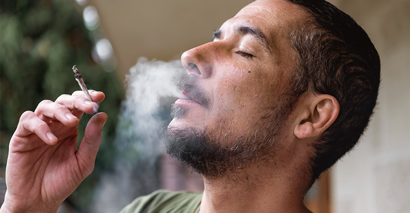 Online-Seminar „Cannabis und Suchtprävention im Unternehmen“: Person raucht einen Joint mit geschlossenen Augen. Online-Seminar „Cannabis und Suchtprävention im Unternehmen“: Person raucht einen Joint mit geschlossenen Augen.