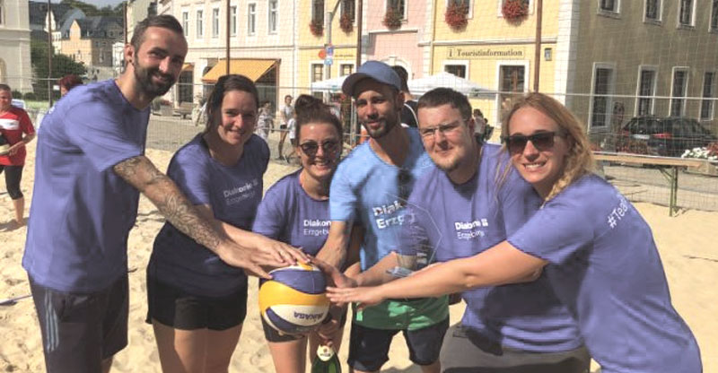 Frau und Männer halten gemeinschaftlich einen Volleyball.