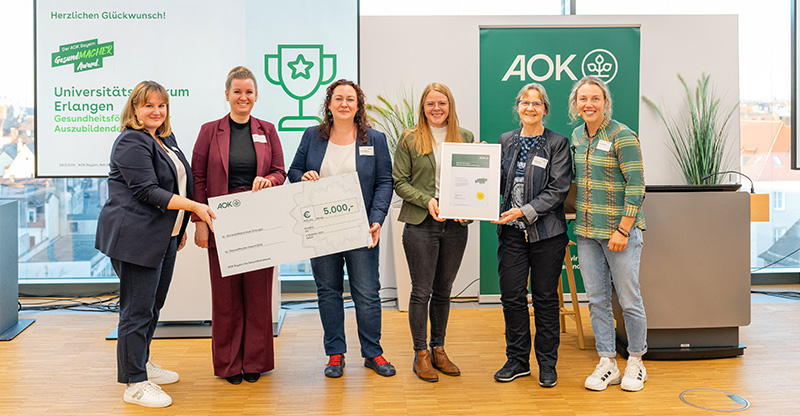 Preisverleihung „GesundMACHER Award“: Eine Gruppe von Frauen präsentiert einen Gewinnerscheck