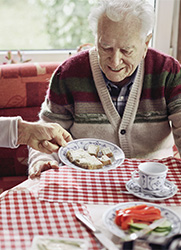 Ein pflegender Angehörige reicht seinem Vater einen Teller mit Brot