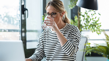 Trink weniger Zucker Eine Frau sitzt am PC und trink aus einem Glas Wasser.
