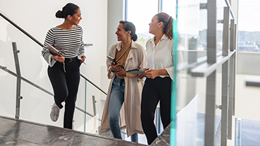 Werde mit jedem Schritt fitter Drei Frauen gehen ein Treppenhaus hoch.