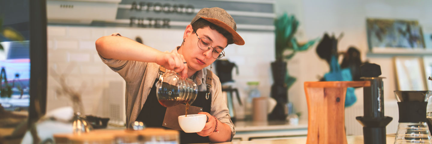 Ein junger Mann gießt Kaffee in eine Tasse. 