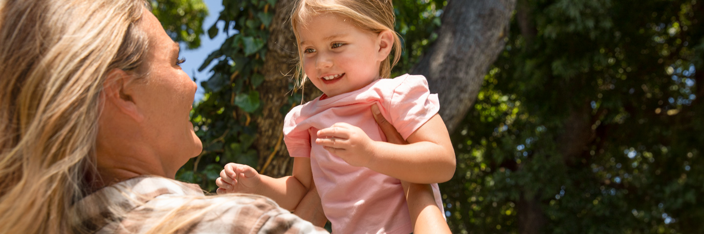 Familienfreundlichkeit in Unternehmen: Eine Frau hebt ein Kind im Park hoch, während ein Mann danebensteht. Familienfreundlichkeit in Unternehmen: Eine Frau hebt ein Kind im Park hoch, während ein Mann danebensteht.