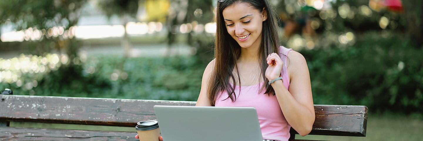 Eine junge Frau sitzt mit Laptop auf einer Bank im Park