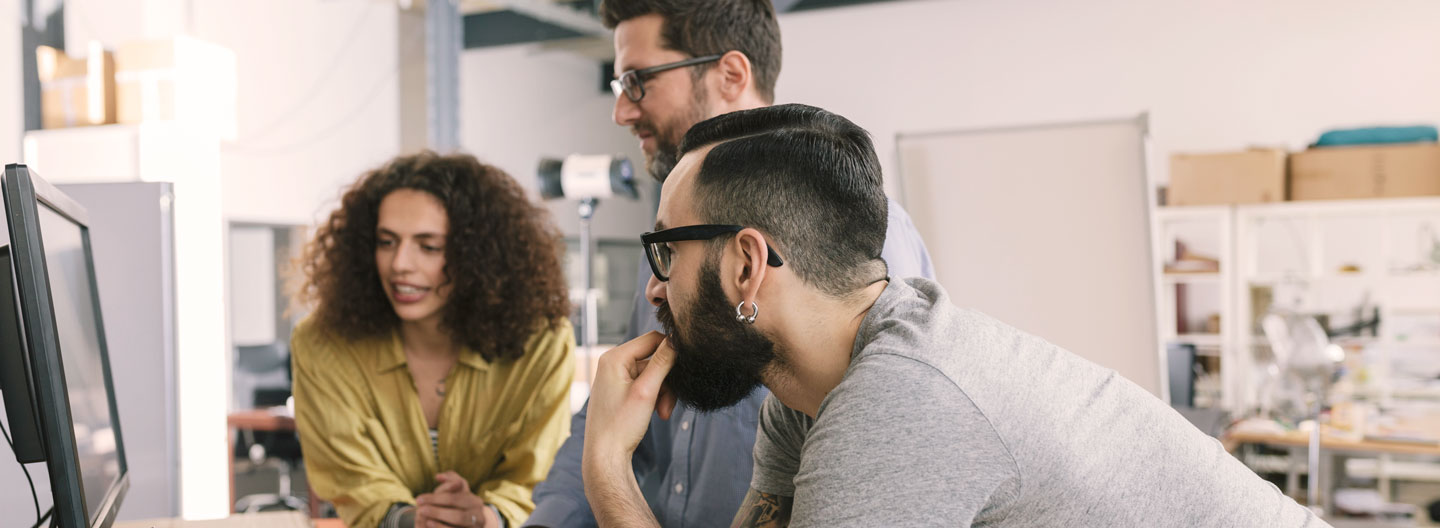 Trends & Tipps zum Jahreswechsel: Drei Personen in einem Büro schauen gemeinsam auf einen Bildschirm.