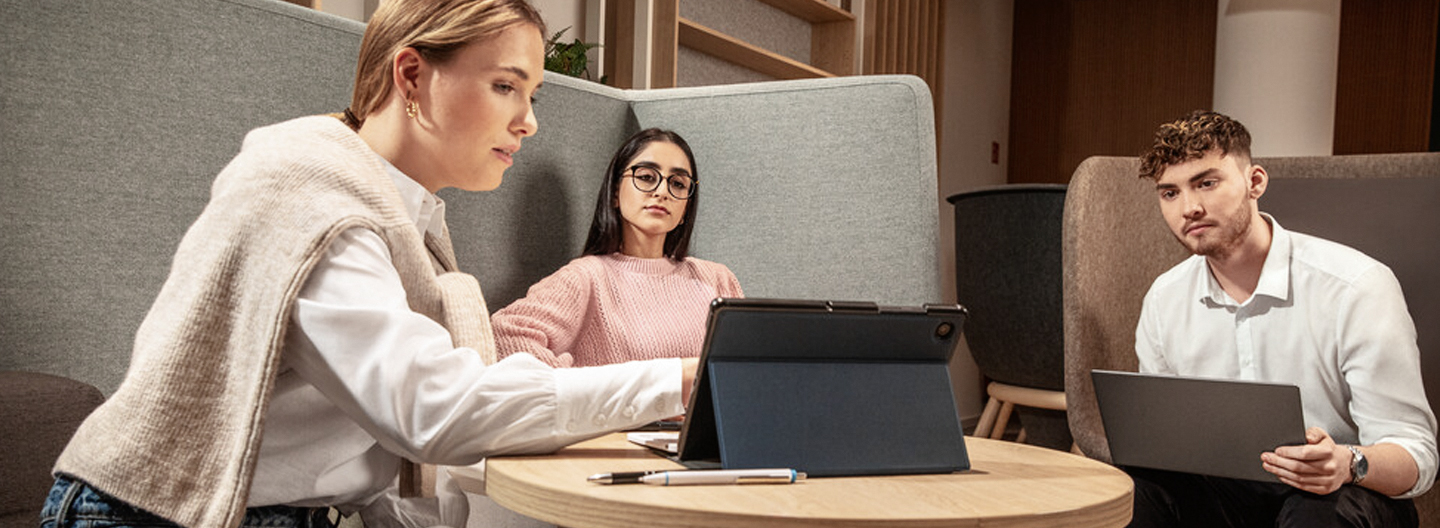 Zwei Frauen und ein Mann sitzen in einer Runde und blicken auf einen Tabletbildschirm.