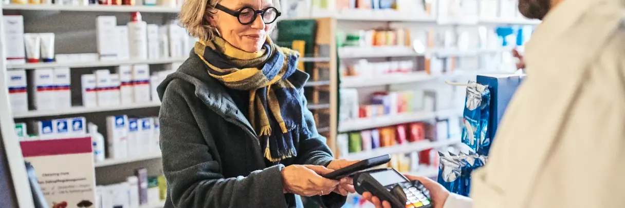 Kundin bezahlt in Apotheke mit ihrem Smartphone. Symbolbild für Digitalisierung in Apotheken. 