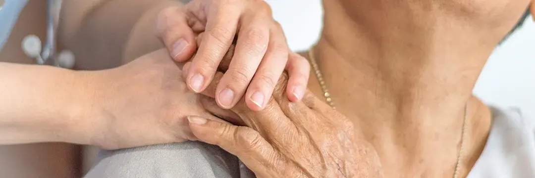 Pflegerin drückt die Hand einer älteren Patientin auf ihrer Schulter