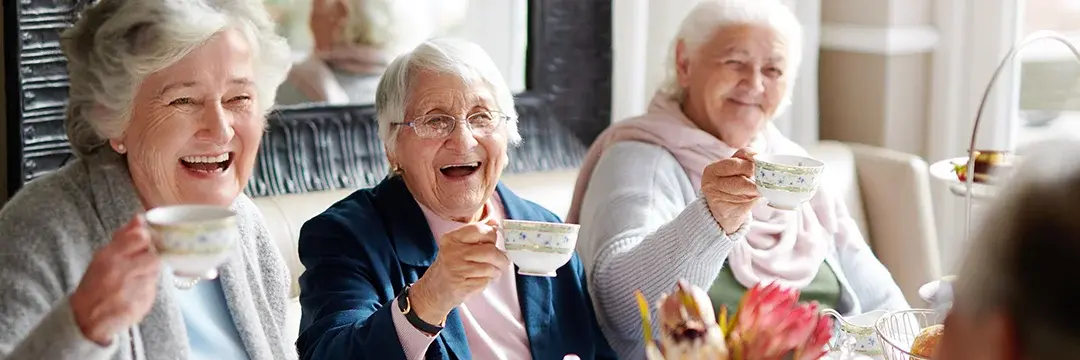 Mehrere ältere Damen sitzen am Tisch. Lachend halten die eine Tasse hoch