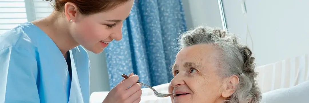 Pflegekraft füttert ältere Dame mit einen Löffel