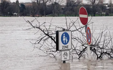 Das Bild zeigt eine überflutetet Straße. Zwei Verkehrsschilder, Durchfahrtverboten sowie Fußgängerweg, sind komplett von Wasser umschlossen.