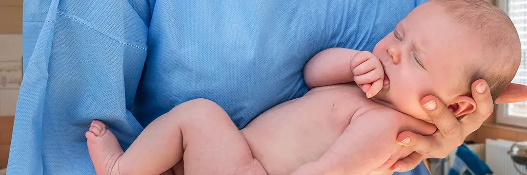 Hebamme hält neugeborenes Baby im Arm
