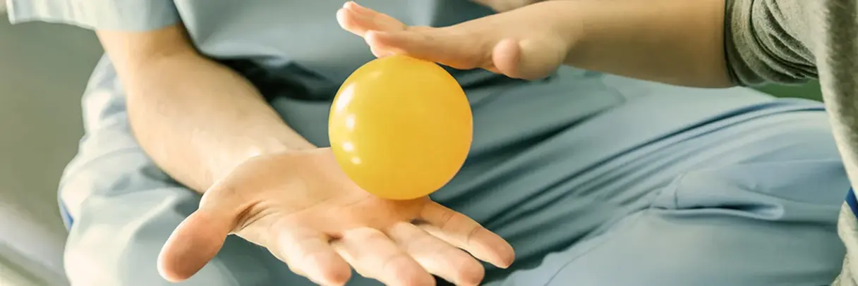 Ergotherapeut und Kind, haben in einer Hand mit einem kleinen Ball und machen Übung