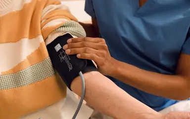 Bildausschnitt zeigt die Blutdruckmessung im Pflegeheim. Eine Pflegekraft legt die Manschette eines Blutdruckmessgeräts an den Arm eines älteren Menschen an.