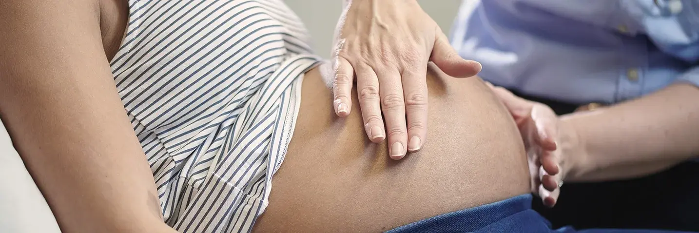 Hebamme tastet Bauch einer schwangeren Frau ab