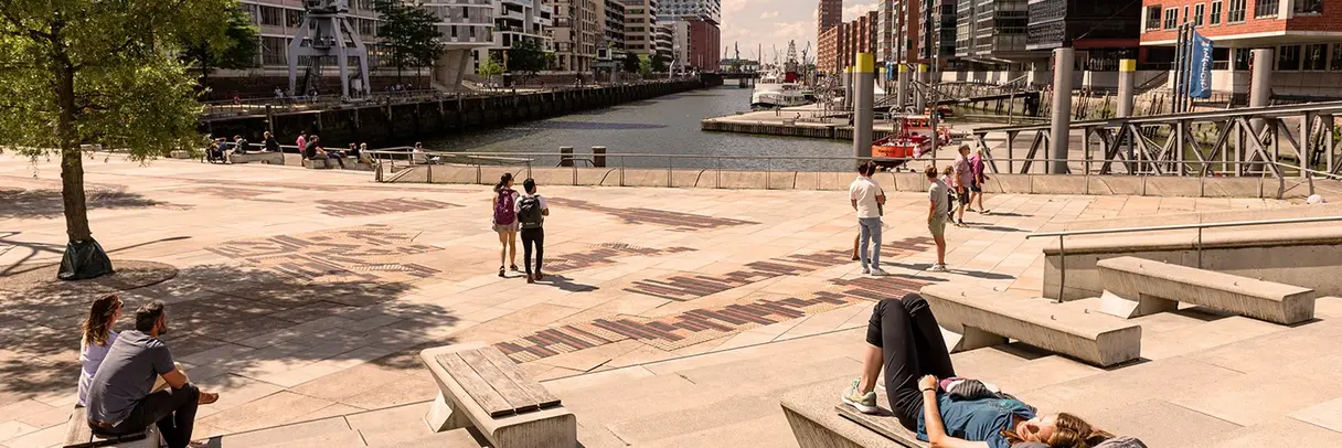 Menschen liegen und sitzen auf den Magellanterrassen in der Sommersonne und blicken auf die Elbphilharmonie und die Hafencity in Hamburg. 