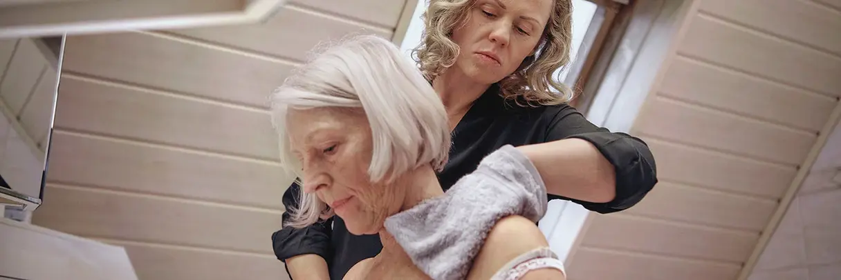 Pflegekraft wäscht mit einem Lappen den Rücken einer älteren Frau