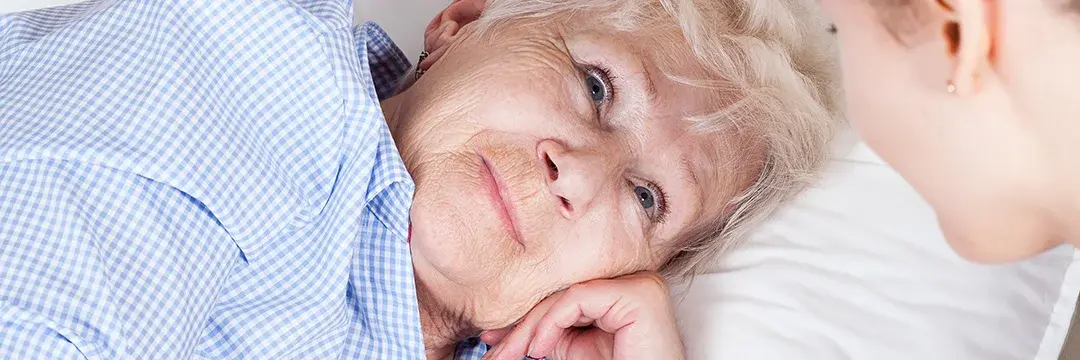 Ältere Frau, die im Bett liegt, schaut freundlich eine Krankenschwester an