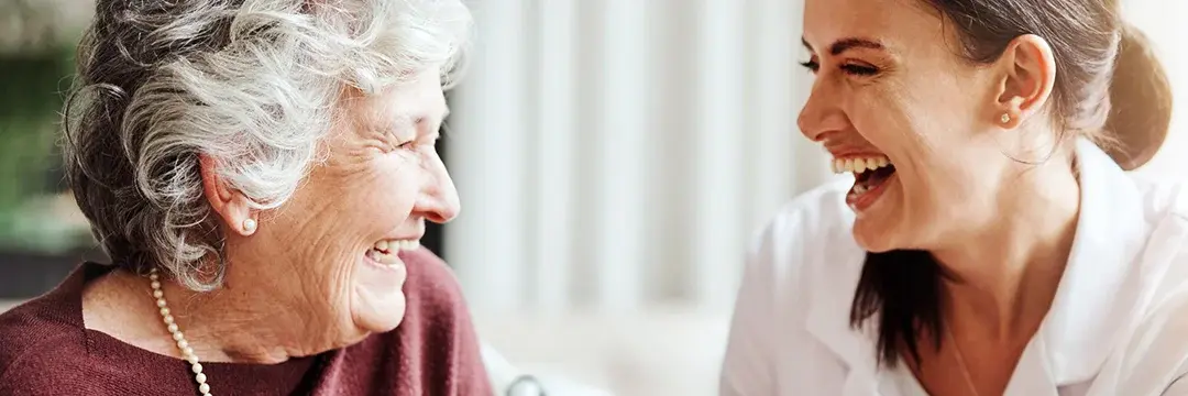 Pflegeheimbewohnerin lacht mit junger Pflegekraft