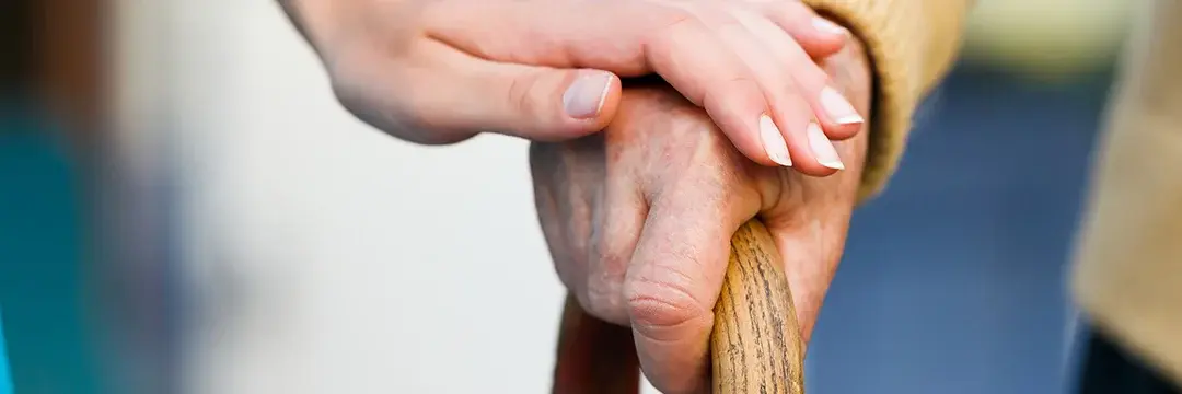 Frau legt ihre Hand auf die eines Senionren der seine Gehilfe hält Frau berührt Senionrenhand auf einer Gehilfe 