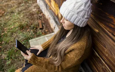 Das Bild zeigt eine junge Frau mit einer Wollmütze, die im Freien ein Smartphone benutzt.