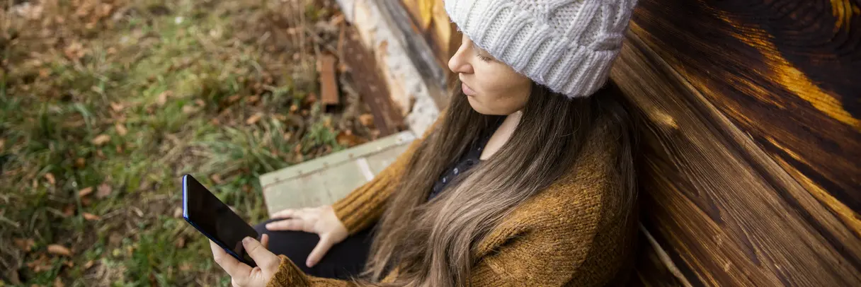 Das Bild zeigt eine junge Frau mit einer Wollmütze, die im Freien ein Smartphone benutzt.