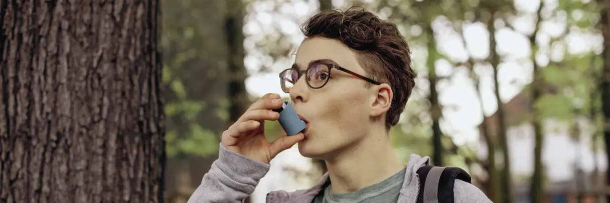 Das bild zeigt einen Teenager, der mit einem Asthma-Spray inhaliert. 