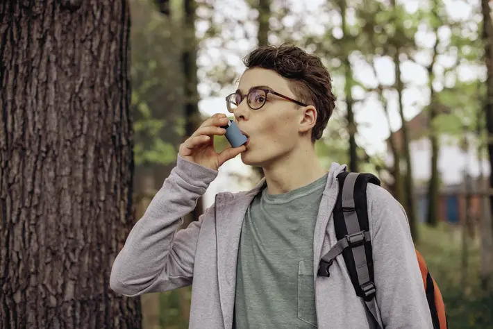 Das bild zeigt einen Teenager, der mit einem Asthma-Spray inhaliert. 