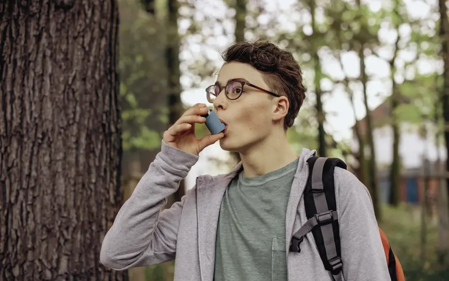 Das bild zeigt einen Teenager, der mit einem Asthma-Spray inhaliert. 