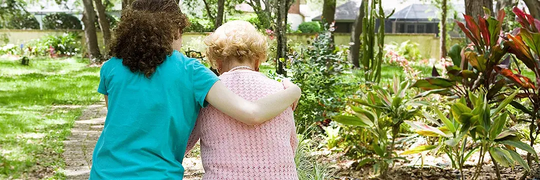 Junge Frau stützt Seniorin beim Waldspaziergang