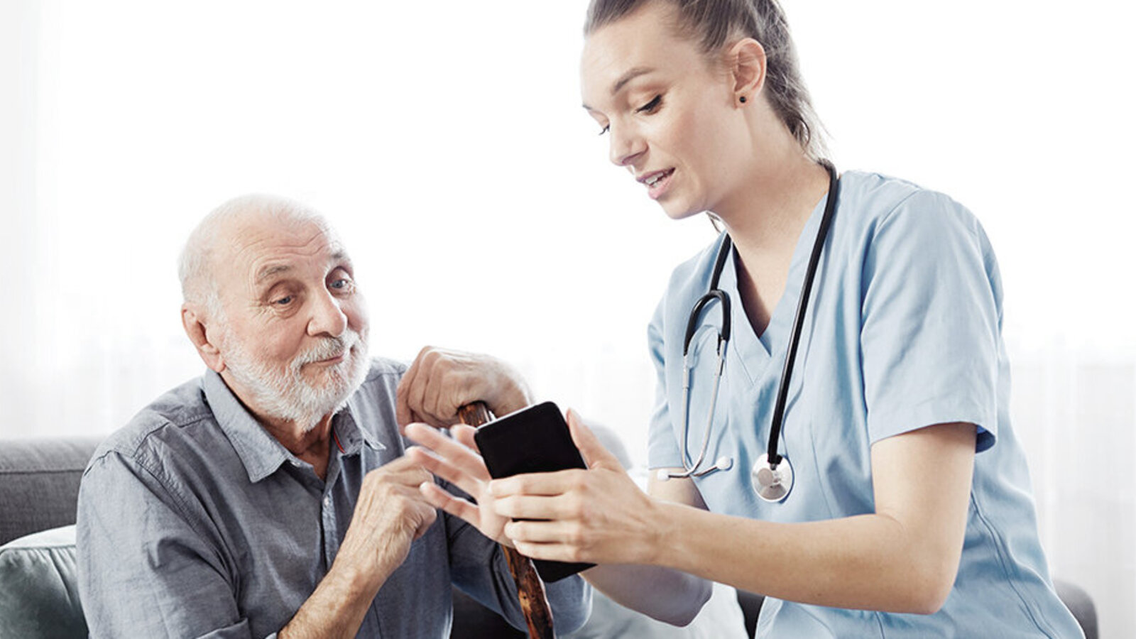 Pflegerin zeigt Senior etwas auf einem Smartphone