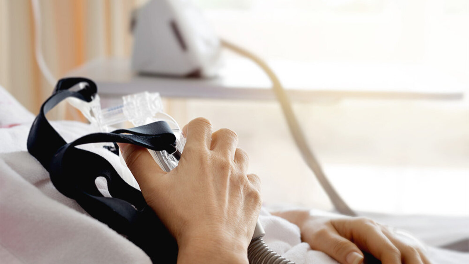 Person im Krankenbett hält eine Beatmungsmaske in der Hand