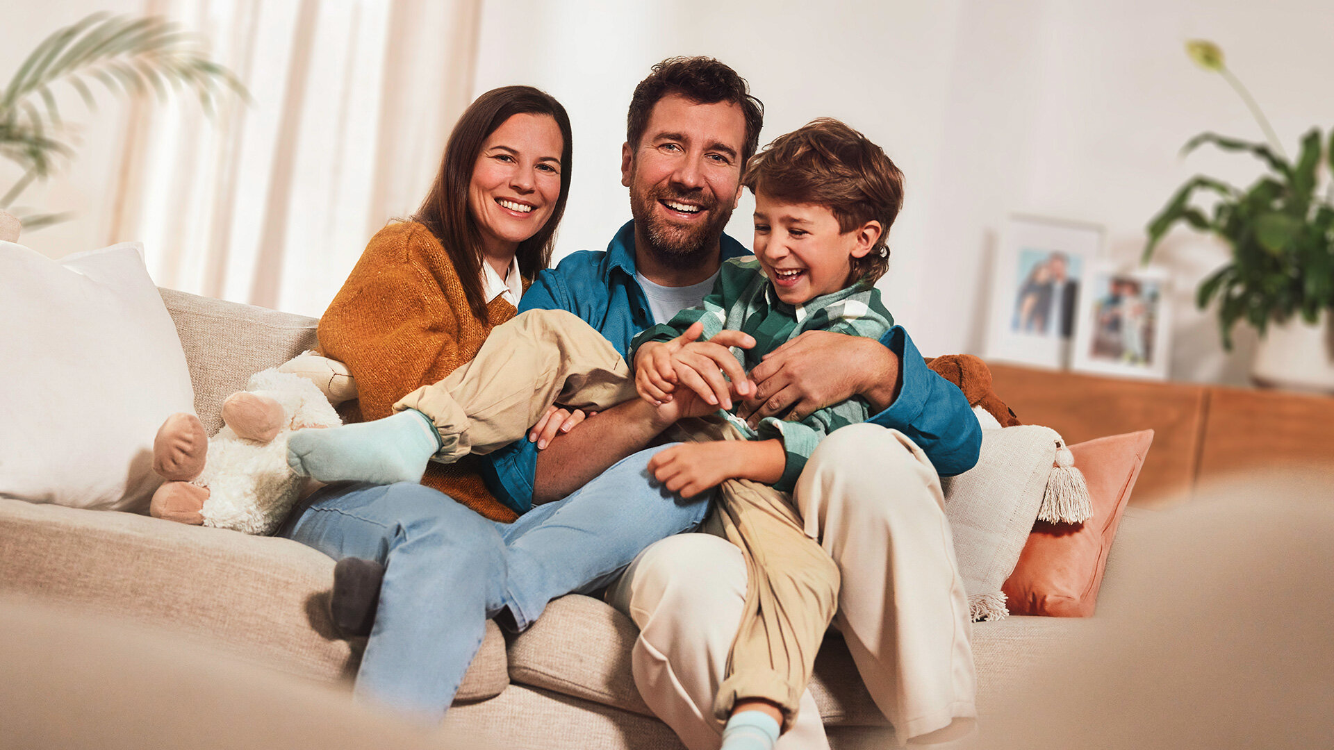 Glückliche Familie bestehend aus Vater, Mutter und Sohn. Lachend auf einem Sofa.