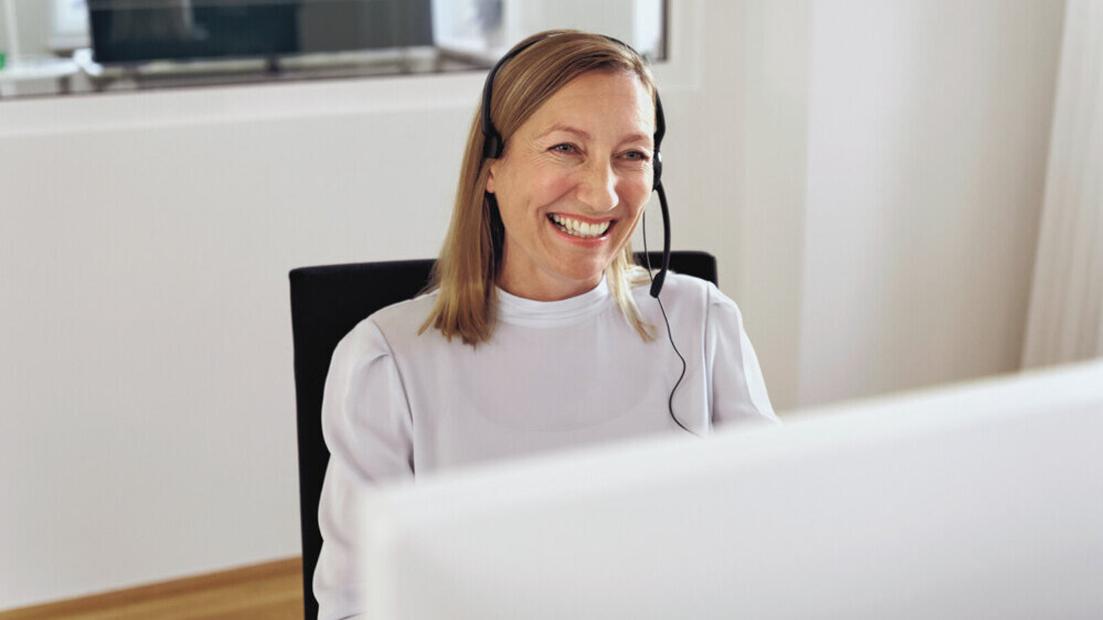Frau sitzt mit Headset am PC und lächelt