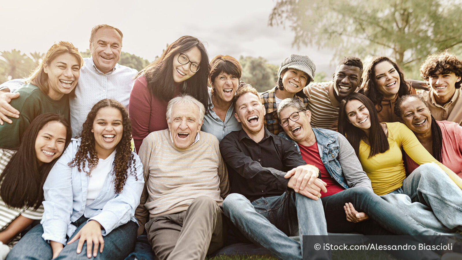 14 Menschen unterschiedlichen Alters und unterschiedlicher Herkunft posieren lachend für ein Gruppenfoto.