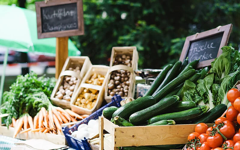 Frisches Gemüse wie Zucchini, Tomaten und Möhren auf einem Marktstand.