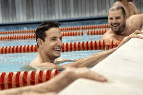 Zwei Männer halten sich am Beckenrand eines Schwimmbeckens fest und lachen. Sie nehmen an einem AOK Gesundheitskurs teil.