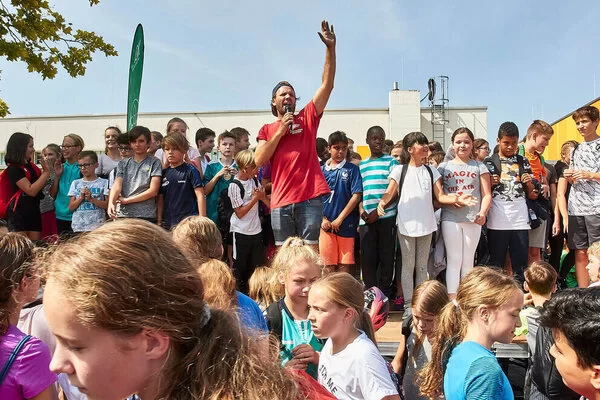 Auf dem Bild ist die Veranstaltung eines Sportvereins mit vielen Kindern und einem erwachsenen Sprecher zu sehen.