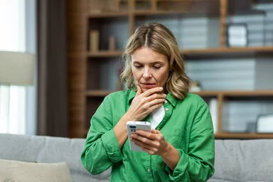 Eine Frau blickt nachdenklich auf ihr Smartphone, das sie in der Hand hält.