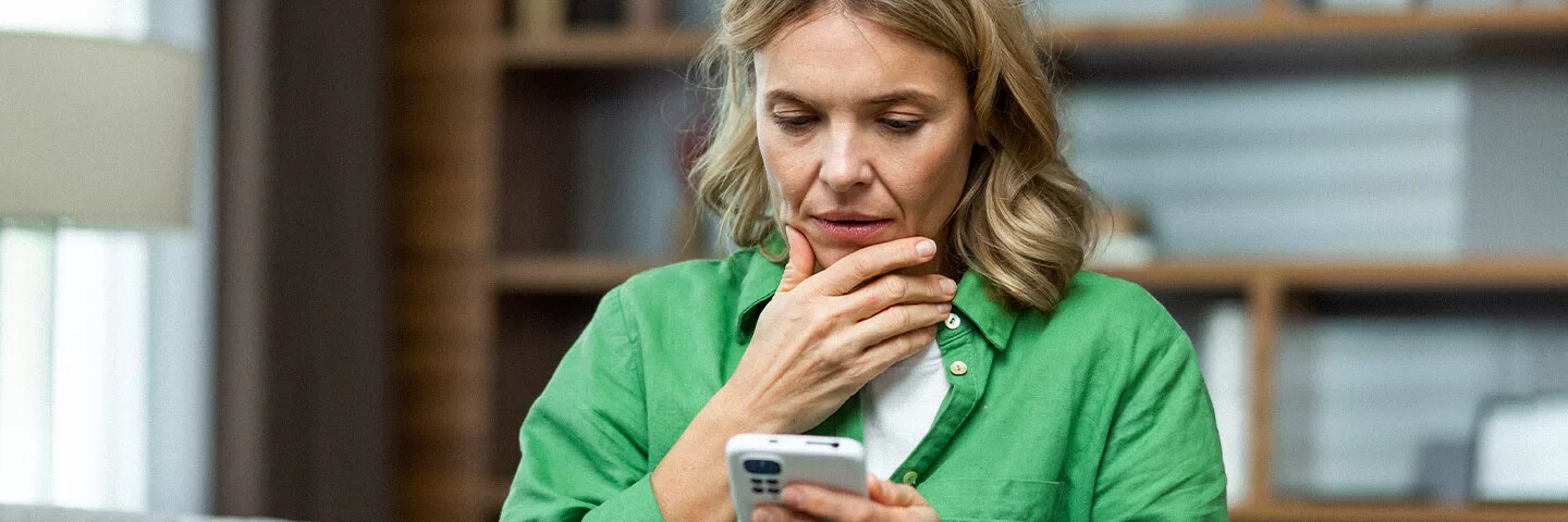 Eine Frau blickt nachdenklich auf ihr Smartphone, das sie in der Hand hält.