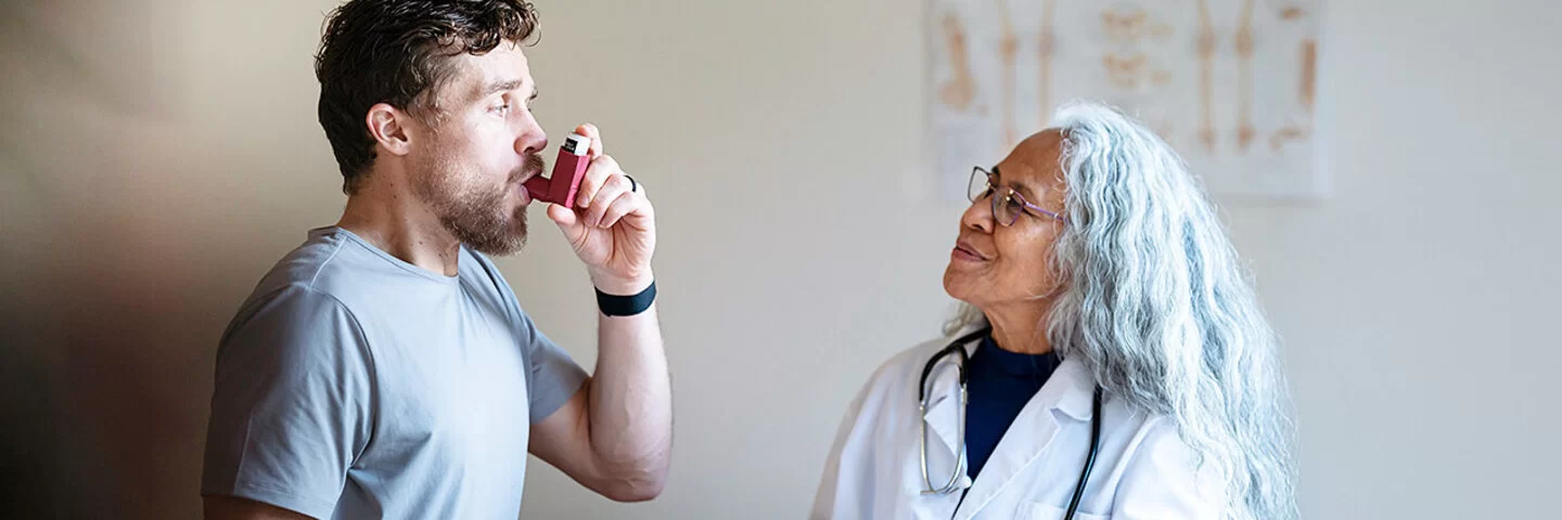 Ein junger Patient mit Asthma verwendet einen Puffer-Inhalator, während er einen Arzttermin mit seiner Ärztin hat.